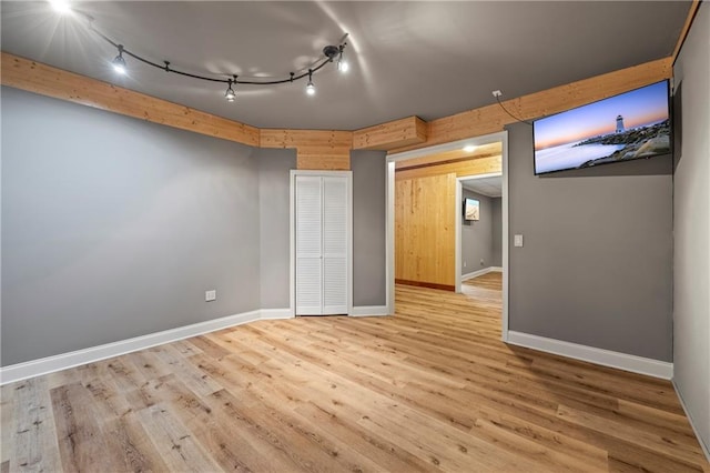 unfurnished bedroom featuring track lighting, wood finished floors, and baseboards