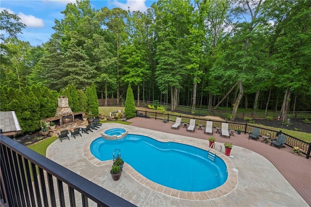 view of swimming pool with an outdoor stone fireplace, a pool with connected hot tub, fence, a deck, and a patio