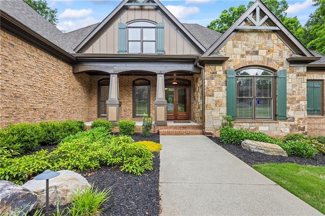 property entrance with board and batten siding, stone siding, covered porch, and a shingled roof