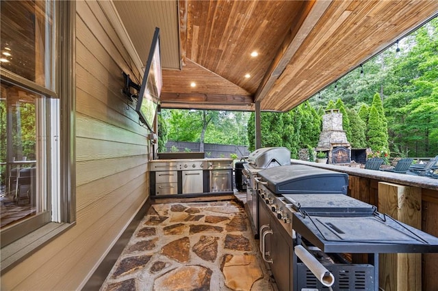 view of patio / terrace with an outdoor kitchen, an outdoor stone fireplace, fence, and grilling area