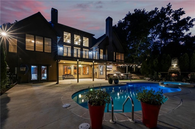 pool at dusk featuring a patio area, an outdoor stone fireplace, french doors, and a pool with connected hot tub