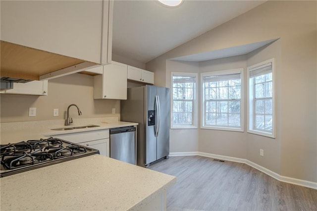 kitchen featuring vaulted ceiling, appliances with stainless steel finishes, sink, white cabinets, and light hardwood / wood-style flooring