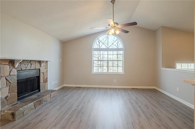 unfurnished living room with lofted ceiling, ceiling fan, a fireplace, wood-type flooring, and a textured ceiling