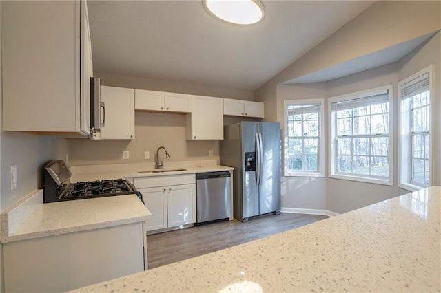 kitchen featuring lofted ceiling, sink, appliances with stainless steel finishes, light stone countertops, and white cabinets