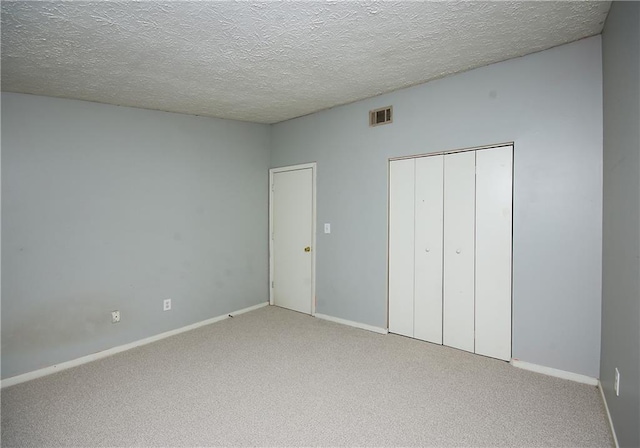 unfurnished bedroom featuring a textured ceiling, a closet, and light carpet