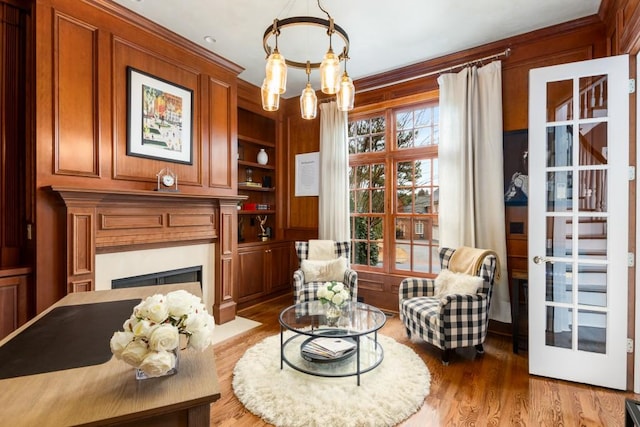 sitting room with wood walls, wood-type flooring, a chandelier, crown molding, and built in shelves