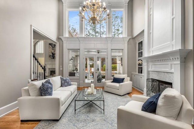 living room with french doors, light hardwood / wood-style flooring, a notable chandelier, a towering ceiling, and a high end fireplace