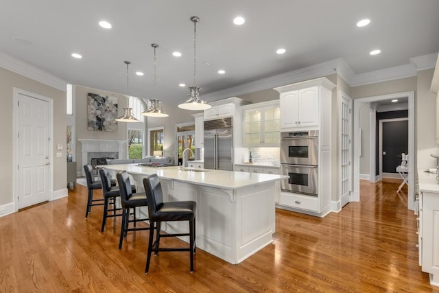 kitchen with appliances with stainless steel finishes, pendant lighting, sink, white cabinets, and a spacious island