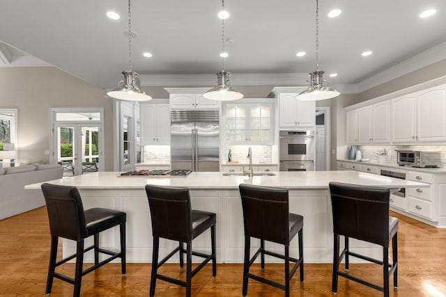 kitchen with white cabinetry, stainless steel appliances, sink, and a large island with sink