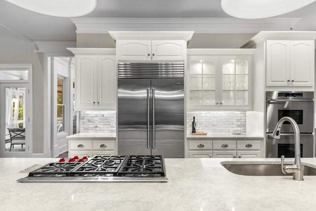 kitchen with sink, appliances with stainless steel finishes, tasteful backsplash, ornamental molding, and white cabinets