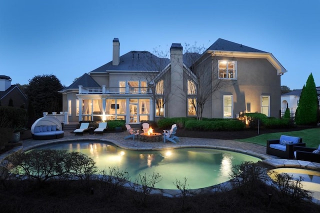 back house at dusk featuring a balcony, a patio area, and a fire pit