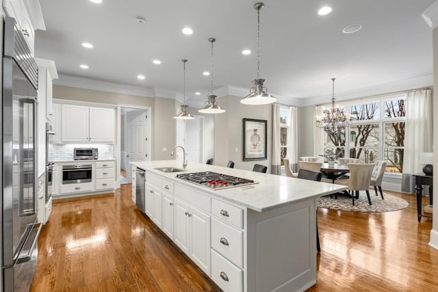 kitchen with sink, decorative light fixtures, an island with sink, stainless steel appliances, and white cabinets