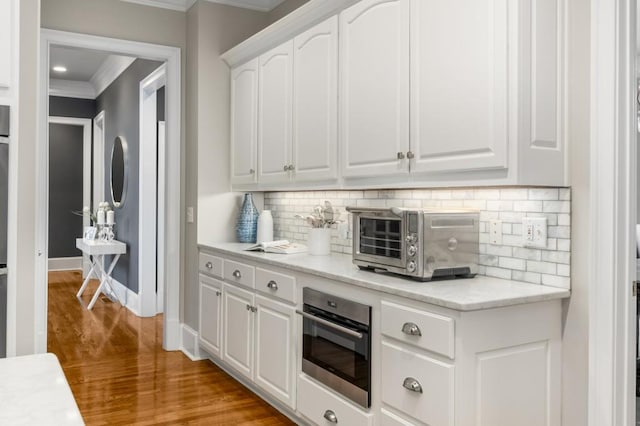 kitchen with tasteful backsplash, white cabinetry, oven, ornamental molding, and light hardwood / wood-style floors