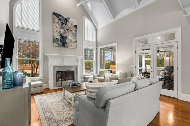 living room with hardwood / wood-style floors, high vaulted ceiling, ceiling fan, a premium fireplace, and french doors