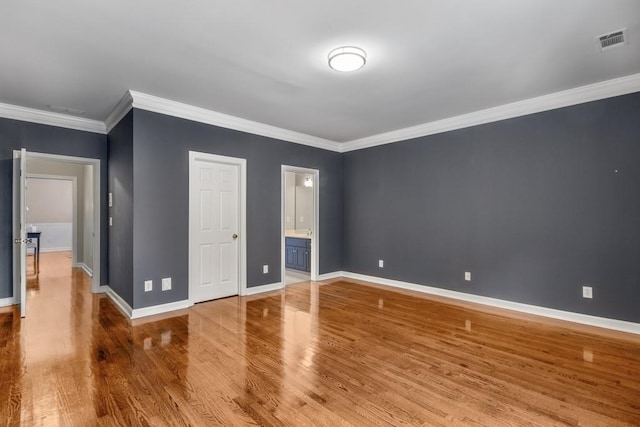 unfurnished bedroom featuring ornamental molding, ensuite bathroom, and hardwood / wood-style floors