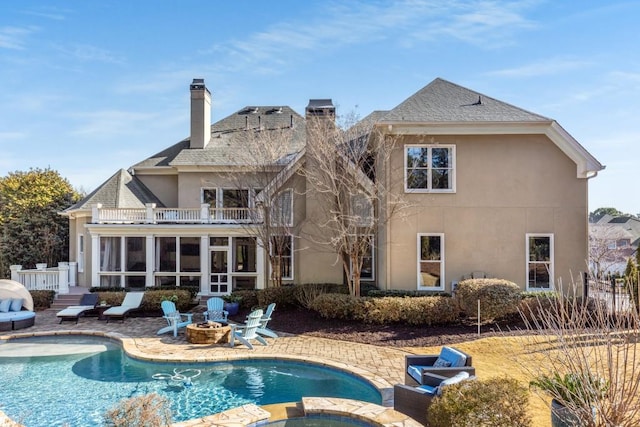 rear view of house featuring a patio, a balcony, a fire pit, a swimming pool with hot tub, and a sunroom