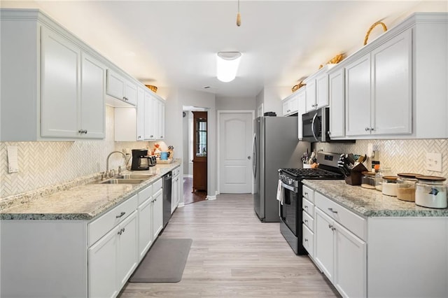kitchen featuring appliances with stainless steel finishes, a sink, backsplash, light wood-style floors, and white cabinetry