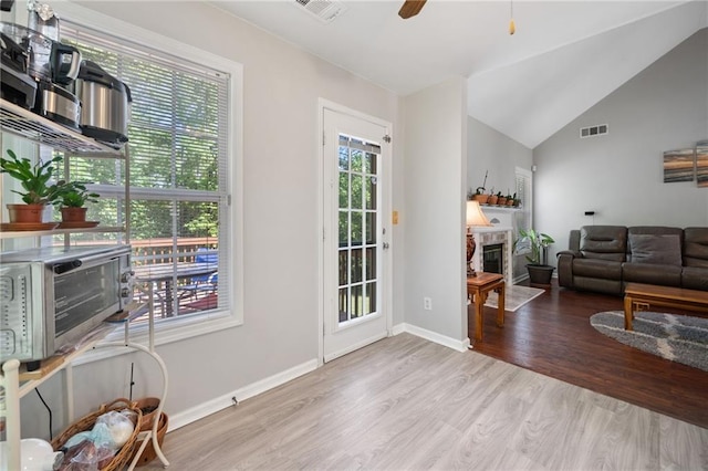entryway with wood finished floors, a glass covered fireplace, ceiling fan, baseboards, and vaulted ceiling