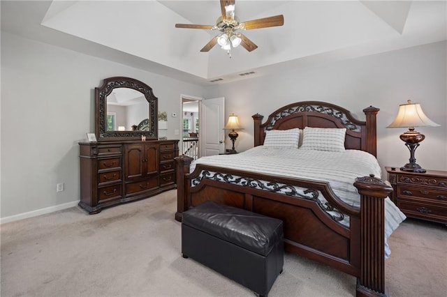 bedroom with a raised ceiling, light carpet, baseboards, and ceiling fan