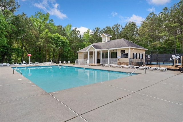 community pool featuring fence, a patio, and view of scattered trees