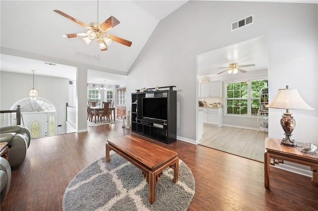 living area featuring high vaulted ceiling, a chandelier, ceiling fan, wood finished floors, and baseboards