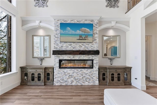 living room featuring a high ceiling, a fireplace, baseboards, and wood finished floors