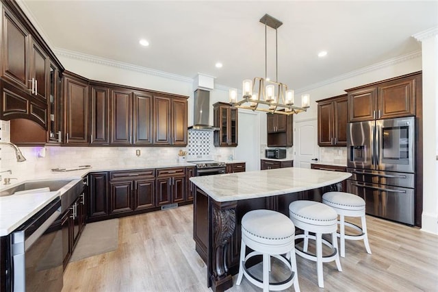 kitchen featuring dark brown cabinetry, stainless steel appliances, a sink, a kitchen island, and wall chimney exhaust hood