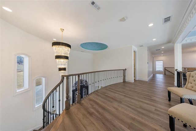 corridor with visible vents, a notable chandelier, an upstairs landing, and wood finished floors