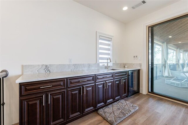 kitchen with visible vents, light wood-style floors, a sink, dark brown cabinets, and beverage cooler