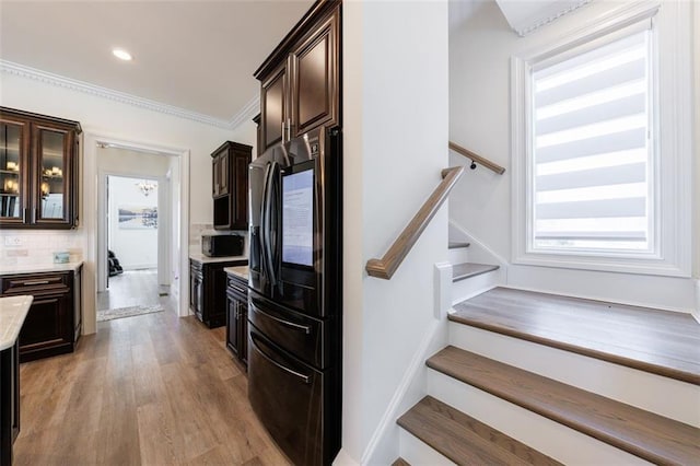 kitchen featuring light wood-style flooring, refrigerator with ice dispenser, dark brown cabinets, light countertops, and tasteful backsplash