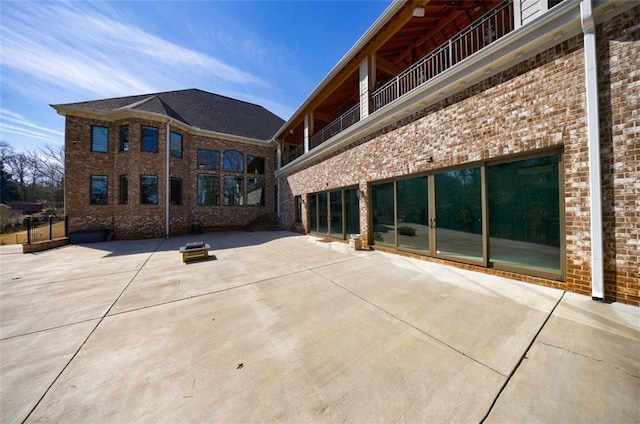 rear view of house with brick siding, a patio, and a balcony