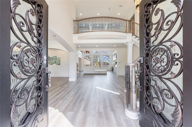 entrance foyer with arched walkways, decorative columns, a towering ceiling, wood finished floors, and baseboards