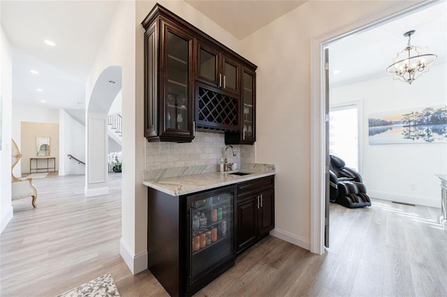 bar with light wood finished floors, beverage cooler, a sink, wet bar, and backsplash