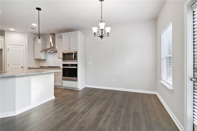 kitchen featuring wall chimney range hood, pendant lighting, decorative backsplash, white cabinets, and appliances with stainless steel finishes