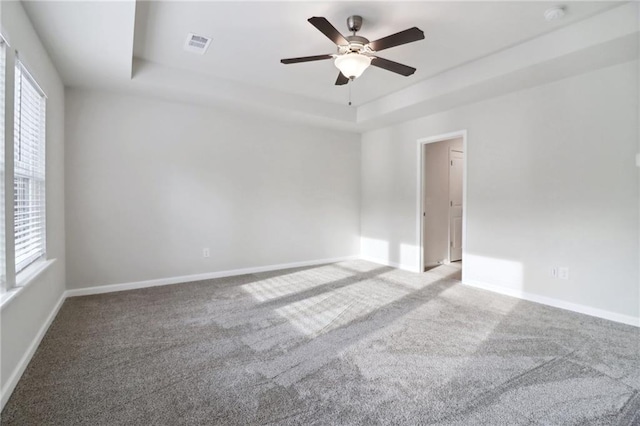 carpeted spare room featuring ceiling fan, a wealth of natural light, and a tray ceiling