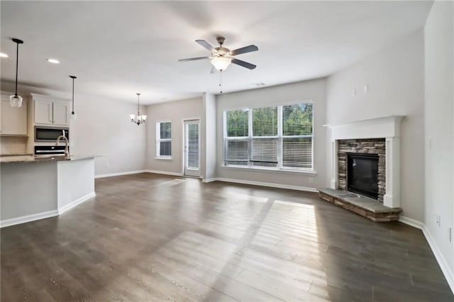 unfurnished living room with a fireplace, ceiling fan with notable chandelier, and dark wood-type flooring