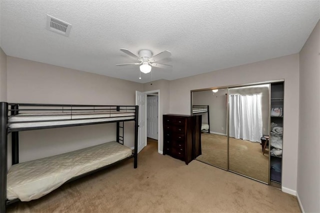 bedroom with ceiling fan, light colored carpet, a textured ceiling, and a closet