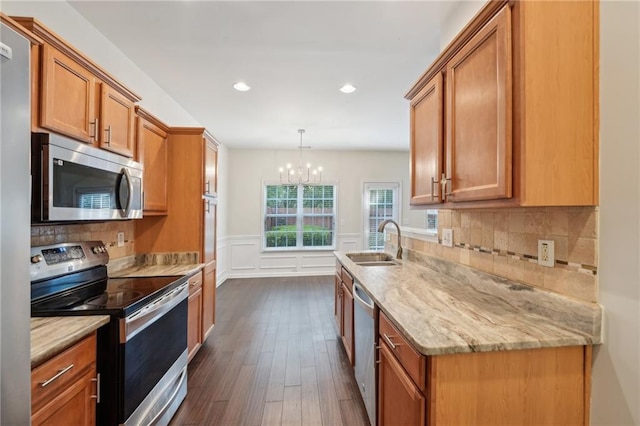kitchen with light stone counters, a sink, brown cabinetry, stainless steel appliances, and dark wood-type flooring