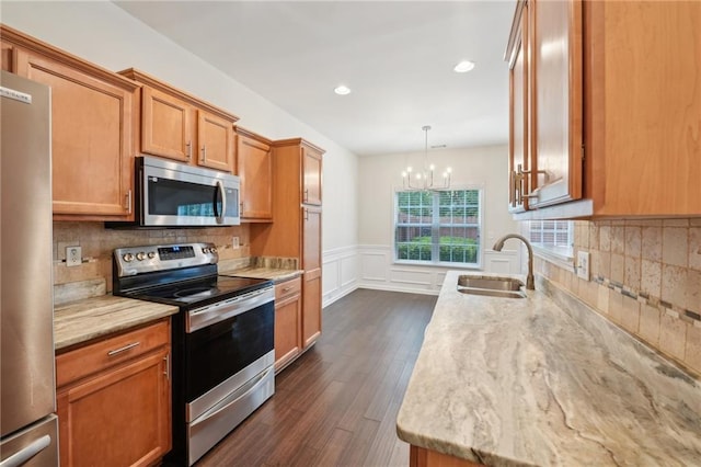 kitchen with light stone counters, a sink, dark wood finished floors, a notable chandelier, and stainless steel appliances