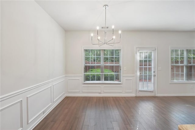 unfurnished dining area featuring a decorative wall, a notable chandelier, hardwood / wood-style flooring, and a wainscoted wall