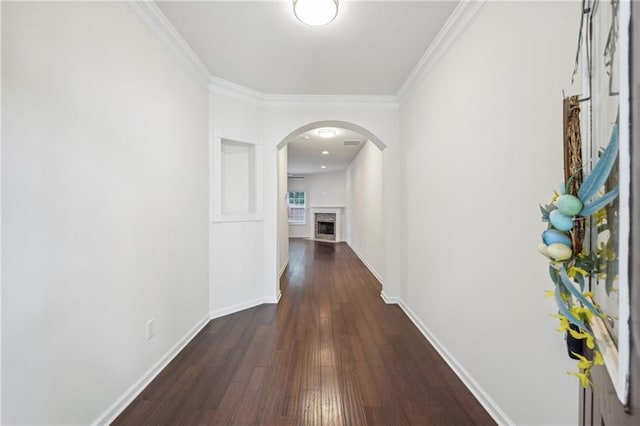 hall with crown molding, arched walkways, baseboards, and dark wood-style floors