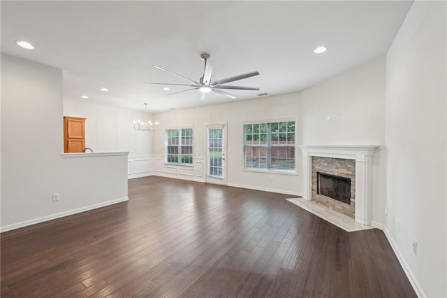 unfurnished living room featuring a stone fireplace, baseboards, dark wood-type flooring, recessed lighting, and ceiling fan with notable chandelier