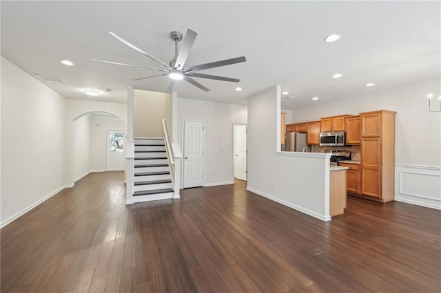 unfurnished living room with a ceiling fan, visible vents, arched walkways, stairs, and dark wood-type flooring