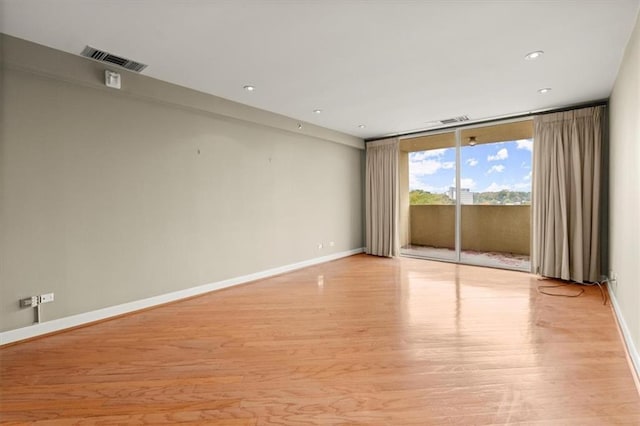 spare room with light wood finished floors, baseboards, visible vents, and a wall of windows