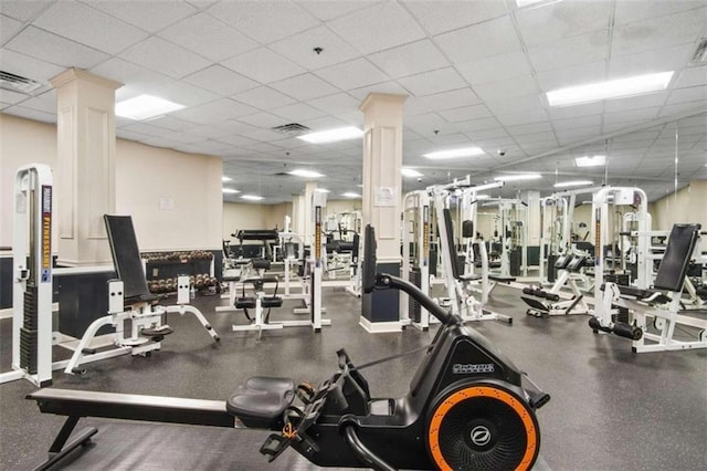 exercise room featuring a paneled ceiling, decorative columns, and visible vents