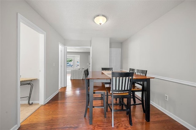 dining space featuring a textured ceiling, wood finished floors, and baseboards