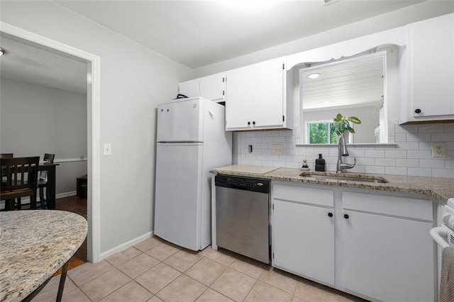 kitchen with stainless steel dishwasher, freestanding refrigerator, a sink, tasteful backsplash, and white cabinets