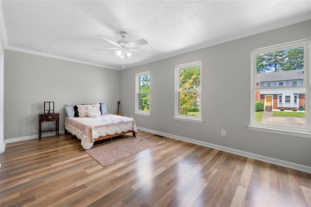 bedroom featuring wood finished floors, a textured ceiling, baseboards, ornamental molding, and ceiling fan