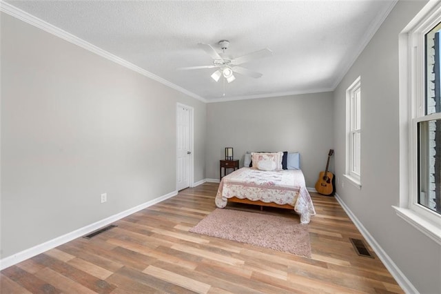 bedroom featuring light wood-type flooring, ornamental molding, baseboards, a textured ceiling, and ceiling fan