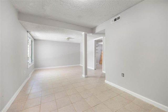 below grade area featuring a textured ceiling, light tile patterned flooring, and baseboards